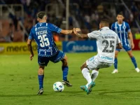 Dua pemain sepak bola berebut bola di lapangan berumput hijau