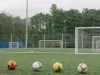 Empat bola sepak berjajar di lapangan rumput dengan gawang latihan di belakangnya
