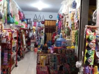 Deretan rak warung kelontong penuh tas, mainan, galon air, dan barang kebutuhan harian