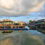Rumah-rumah panggung Suku Bajau berjajar di atas air dengan langit berawan