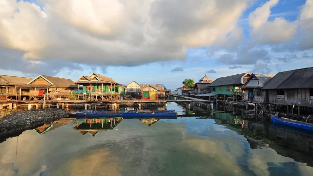 Rumah-rumah panggung Suku Bajau berjajar di atas air dengan langit berawan