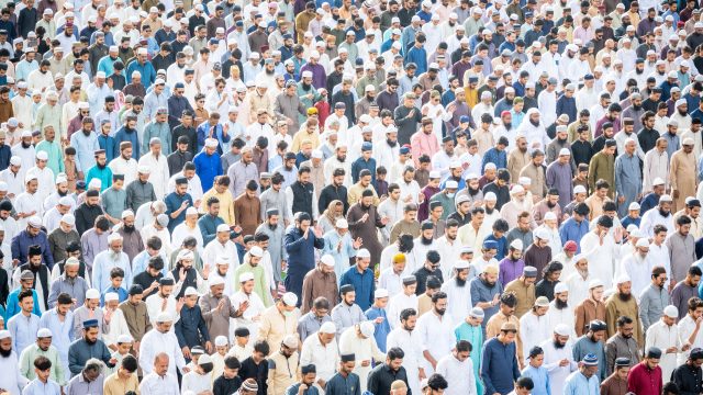 Ilustrasi ribuan orang berbaris rapat mengikuti salat berjamaah di lapangan terbuka.