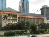 Gedung Bank Indonesia beratap limas di tepi jalan dengan gedung tinggi di belakangnya