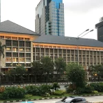 Gedung Bank Indonesia beratap limas di tepi jalan dengan gedung tinggi di belakangnya