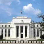Gedung Eccles kantor pusat Federal Reserve berfasad putih dengan bendera Amerika Serikat