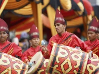 Pemain gandang Minangkabau berbaju merah dan bertopi tinggi menabuh gendang bermotif