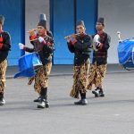 Ilustrasi kelompok pemusik berbusana tradisional memainkan gendang dalam arak-arakan.
