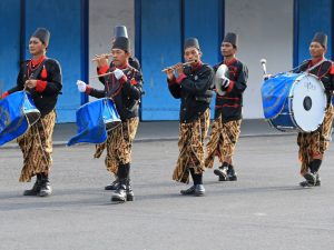 Ilustrasi kelompok pemusik berbusana tradisional memainkan gendang dalam arak-arakan.