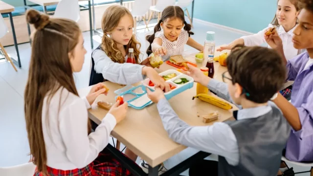 Sekelompok anak duduk semeja menyantap makanan di kantin sekolah