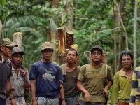 Sekelompok laki-laki berdiri di dalam hutan sambil menggendong kayu dan keranjang anyaman