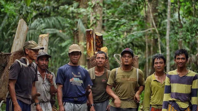 Sekelompok laki-laki berdiri di dalam hutan sambil menggendong kayu dan keranjang anyaman
