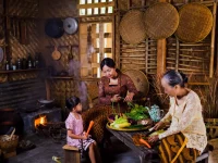 Ibu, anak perempuan, dan nenek menyiangi sayuran di dapur tradisional berdinding bambu