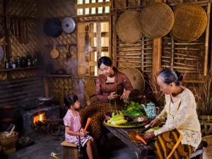 Ibu, anak perempuan, dan nenek menyiangi sayuran di dapur tradisional berdinding bambu