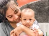 Ibu tersenyum memeluk bayi perempuannya di luar rumah, Yogyakarta
