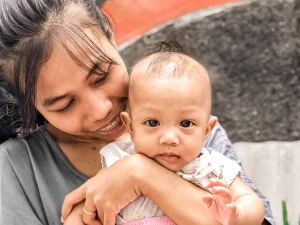 Ibu tersenyum memeluk bayi perempuannya di luar rumah, Yogyakarta