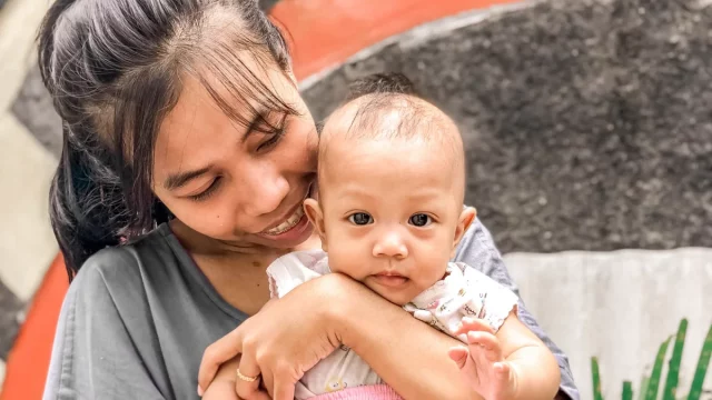 Ibu tersenyum memeluk bayi perempuannya di luar rumah, Yogyakarta