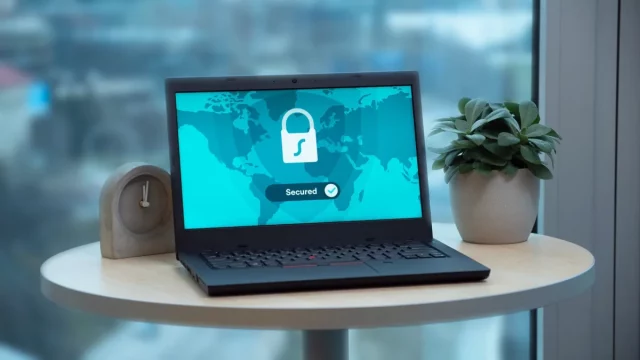 Ilustrasi laptop menampilkan ikon gembok keamanan di atas meja bundar