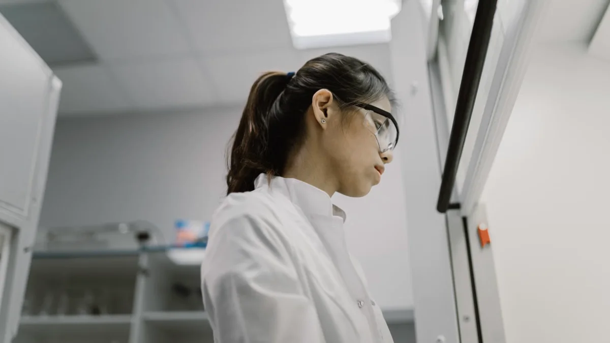 Ilustrasi peneliti perempuan berjas laboratorium dan berkacamata pelindung bekerja di laboratorium