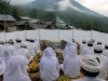 Ilustrasi warga berpakaian putih duduk bersila menghadap sesaji pisang di lereng gunung berkabut