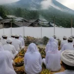 Ilustrasi warga berpakaian putih duduk bersila menghadap sesaji pisang di lereng gunung berkabut