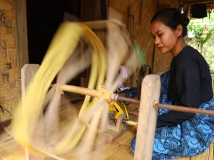 Ilustrasi perempuan memintal benang dengan roda pintal tradisional di Banten