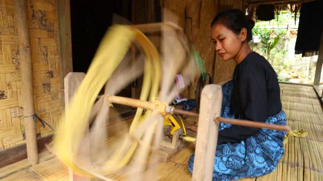 Ilustrasi perempuan memintal benang dengan roda pintal tradisional di Banten