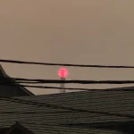Matahari tampak merah samar di balik kabut asap tebal di atas atap-atap rumah