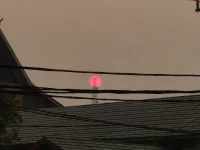Matahari tampak merah samar di balik kabut asap tebal di atas atap-atap rumah