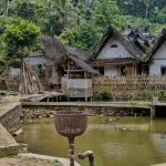 Ilustrasi rumah-rumah beratap ijuk berpagar bambu di tepi kolam di sebuah kampung tradisional
