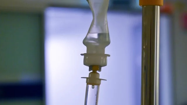 Tabung tetes infus bening menggantung di samping tiang infus di ruang rawat rumah sakit