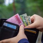 Ilustrasi tangan membuka dompet berisi lembaran uang rupiah dan kartu.