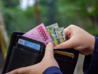 Ilustrasi tangan membuka dompet berisi lembaran uang rupiah dan kartu.