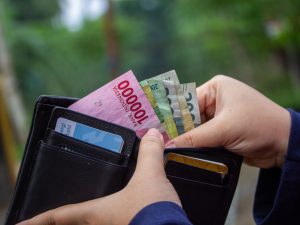 Ilustrasi tangan membuka dompet berisi lembaran uang rupiah dan kartu.