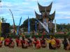 Para pemain randai duduk melingkar di halaman berumput di depan bangunan beratap gonjong saat pertunjukan berlangsung.