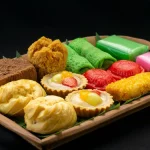 Aneka kue tradisional berwarna-warni tertata di atas nampan kayu berlatar gelap