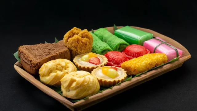 Aneka kue tradisional berwarna-warni tertata di atas nampan kayu berlatar gelap