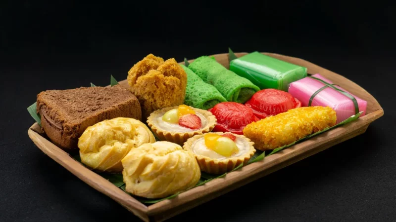 Aneka kue tradisional berwarna-warni tertata di atas nampan kayu berlatar gelap