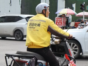 Kurir Meituan berjaket kuning mengendarai skuter listrik mengantar makanan di jalan kota, China