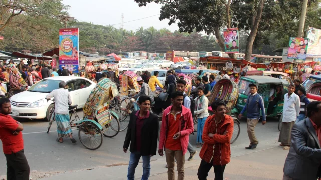 Kerumunan pejalan kaki, becak, dan mobil memadati jalan Kota Dhaka, Bangladesh, pada siang hari