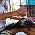Tangan penenun merapikan benang kain tenun ikat hitam putih di alat tenun gedogan