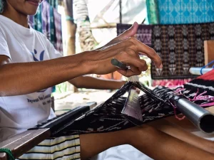Tangan penenun merapikan benang kain tenun ikat hitam putih di alat tenun gedogan