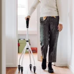 Seorang lanjut usia berjalan di dalam rumah menggunakan alat bantu rollator