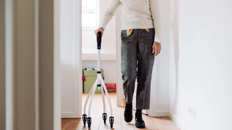 Seorang lanjut usia berjalan di dalam rumah menggunakan alat bantu rollator