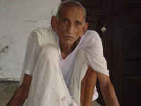 Lelaki lansia berpakaian putih duduk di beranda rumah desa di Chandesh, India