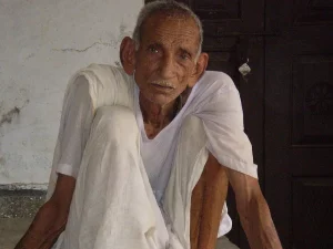 Lelaki lansia berpakaian putih duduk di beranda rumah desa di Chandesh, India
