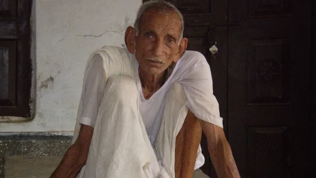 Lelaki lansia berpakaian putih duduk di beranda rumah desa di Chandesh, India