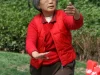 Perempuan lansia mengenakan rompi merah berlatih gerakan tai chi di taman terbuka