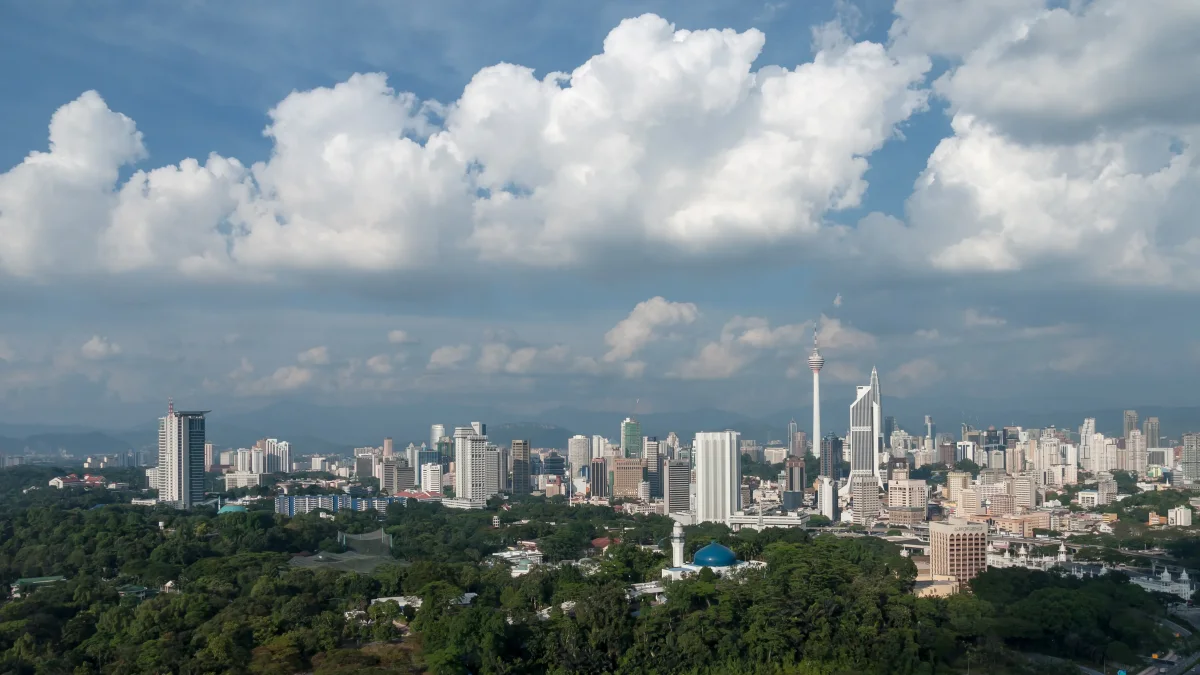 Deretan gedung tinggi Kuala Lumpur di balik hamparan pepohonan di bawah langit berawan