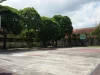 Lapangan futsal terbuka yang kosong dengan ring basket dikelilingi pepohonan dan gedung sekolah