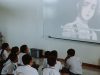 Ilustrasi murid-murid berseragam menonton tayangan dari proyektor di dalam kelas.